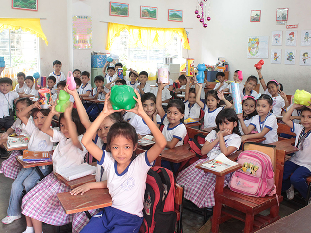 Students in a classroom holding up piggy banks